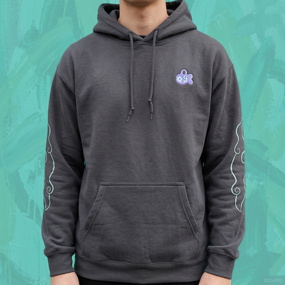 A person wearing a dark gray pullover hoodie with a small icon form Amiko Legends graphic on the left chest and white decorative swirl patterns on both sleeves, set against a textured teal background.